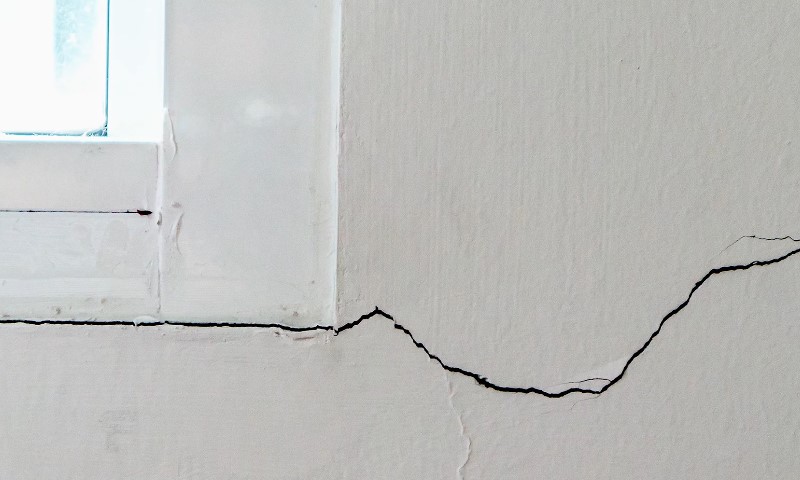 A crack in the wall of a room, with a window visible in the background