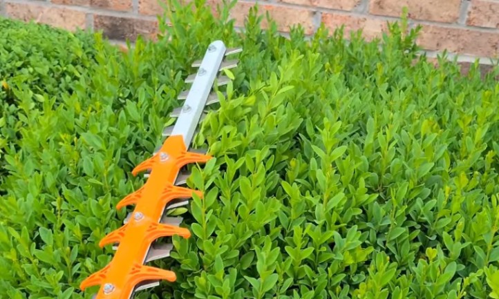 Hedge trimmer featuring a large orange handle, designed for efficient trimming of hedges and shrubs