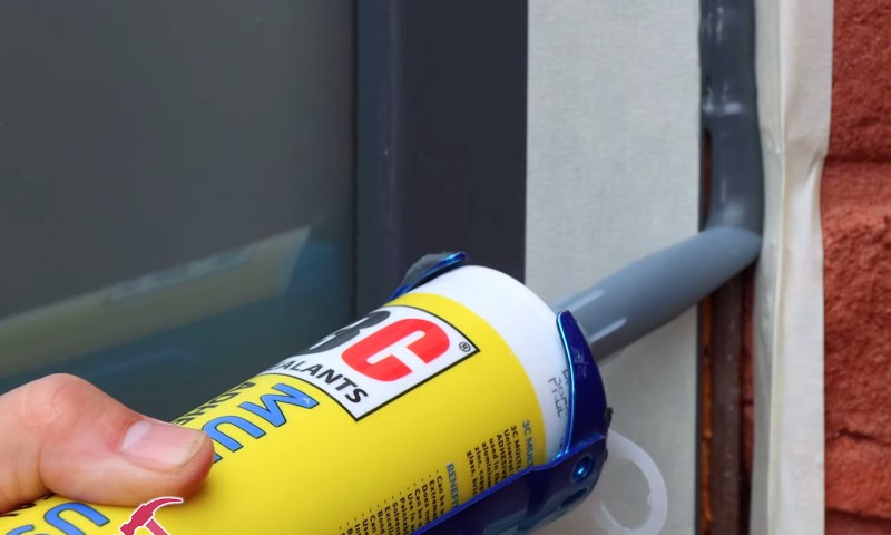 A person applies sealant to a window using a blue tube