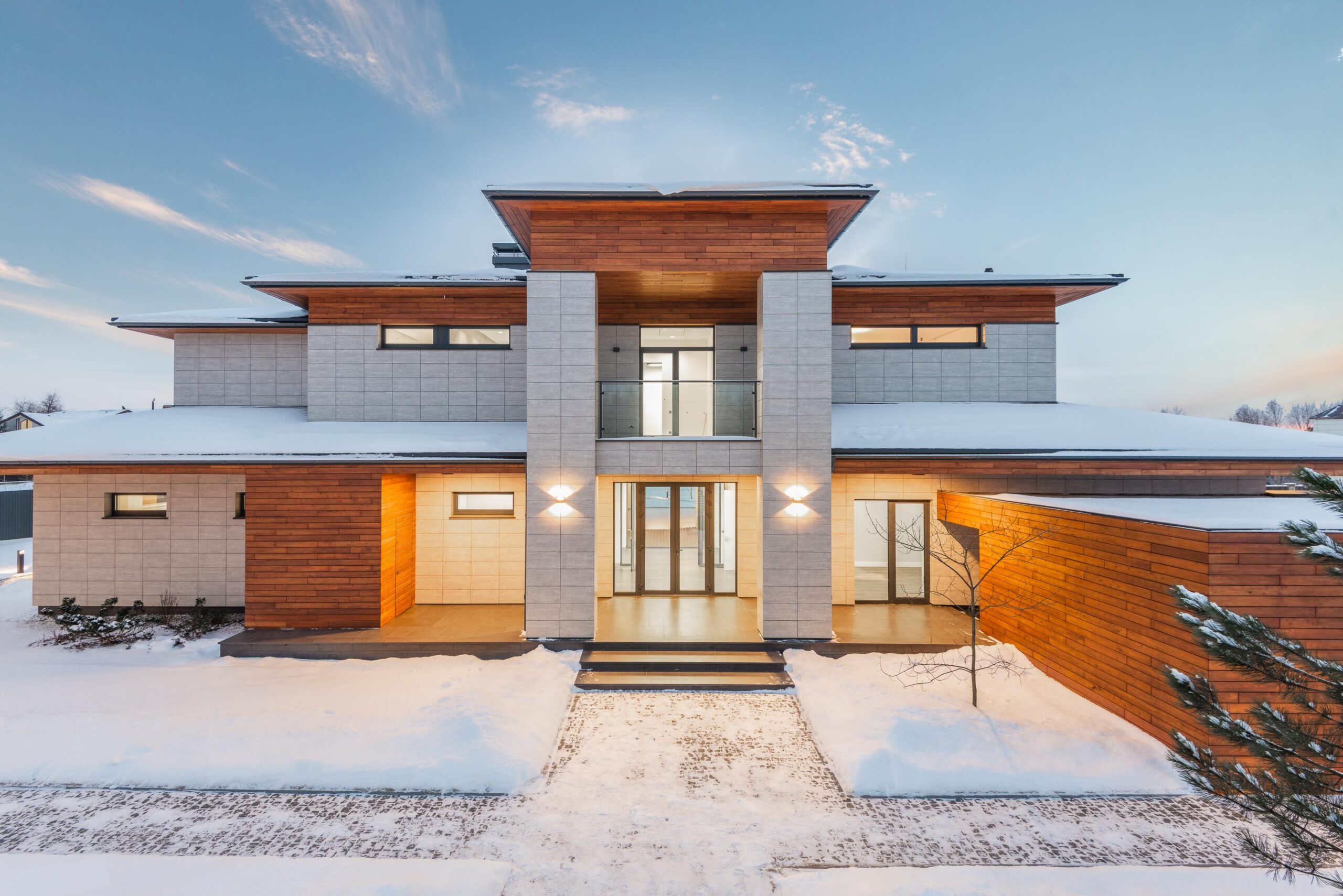 Modern cottage house exterior with mixed stone and wooden facade panels in a winter countryside setting