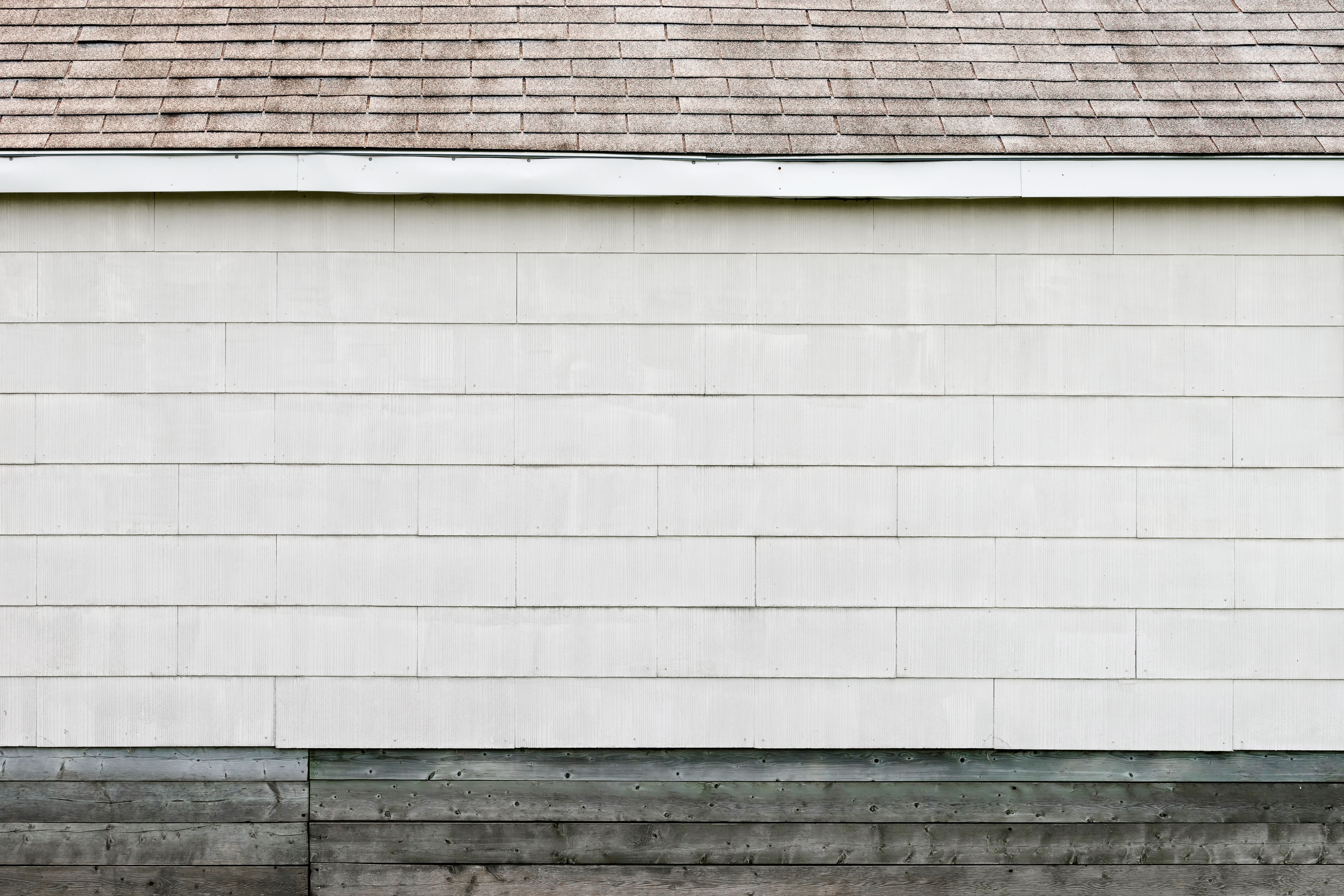 Minimalist exterior wall with white siding and a shingled roof on a clean-lined home